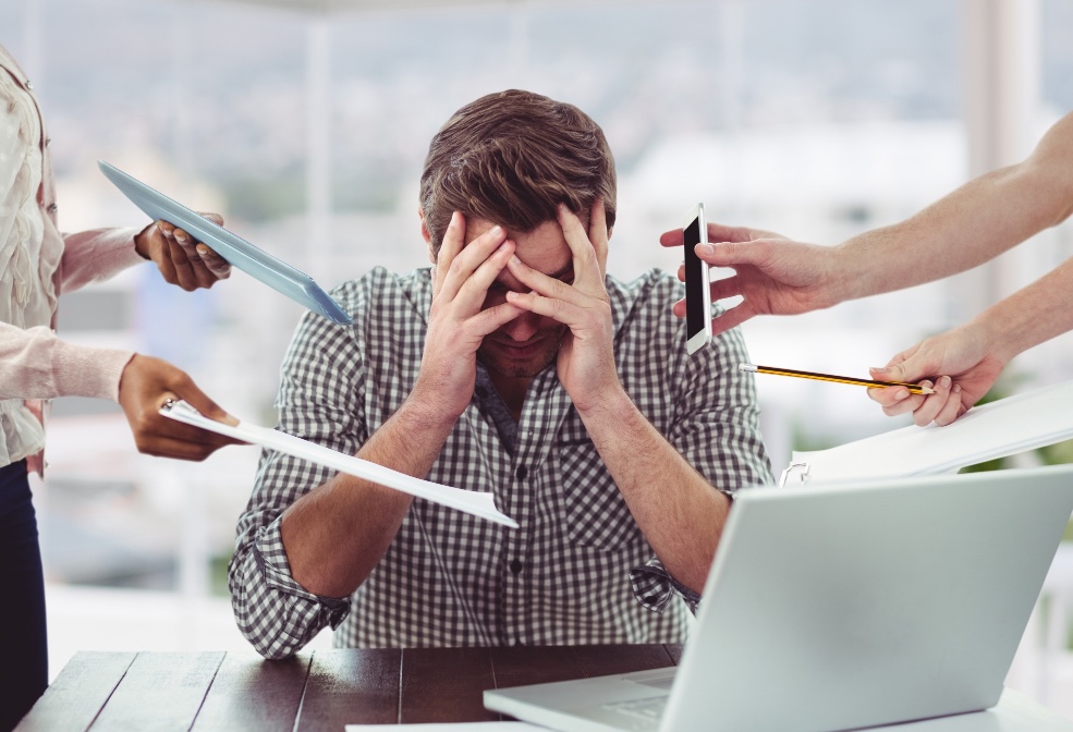 Homme au bureau, soumis à de multiples sollicitations, la tête entre les mains.