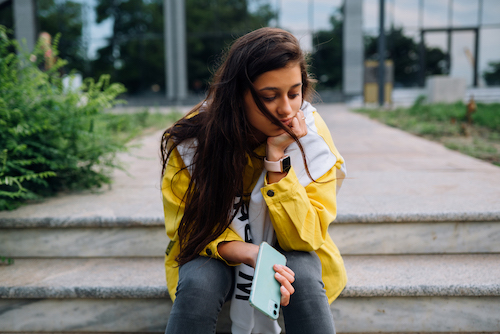 Jeune femme assise sur les marches d'un escalier, l'air triste et le regard dans le vague.